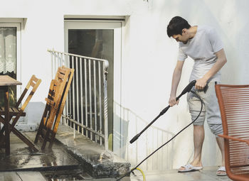 A caucasian guy washes a curb with a metal fence with a pressure of water