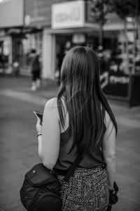 Rear view of woman standing on footpath in city