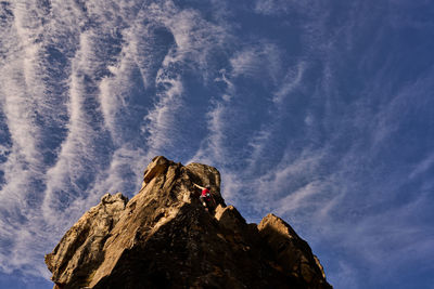 Low angle full length of active senior woman climbing on rocky cliff against sky