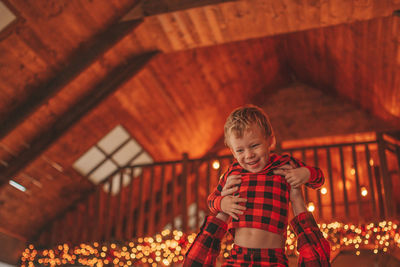 Candid authentic happy dad and son in red plaid pajamas fooling around at wood lodge xmas decorated