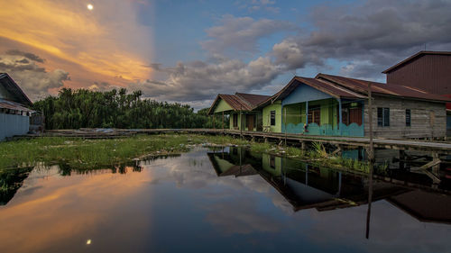 Houses by lake against sky during sunset