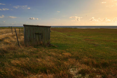 Wooden posts on field by sea against sky