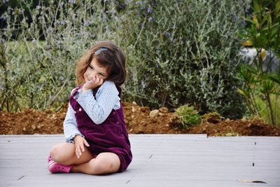 Cute girl sitting on boardwalk against plants