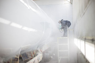 Industrial worker spray painting and wearing protective clothing