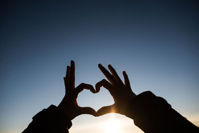 Cropped silhouette hands of woman making heart shape against sky during sunset