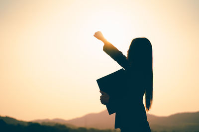 Side view of silhouette woman standing against sky during sunset