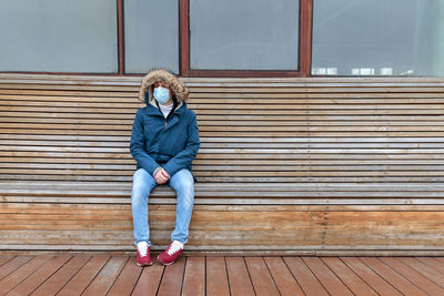 Full length of man wearing mask while sitting on bench