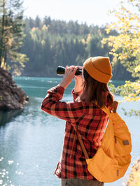 Side view of woman photographing while standing against lake