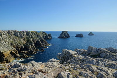 Scenic view of rocks in sea against clear blue sky