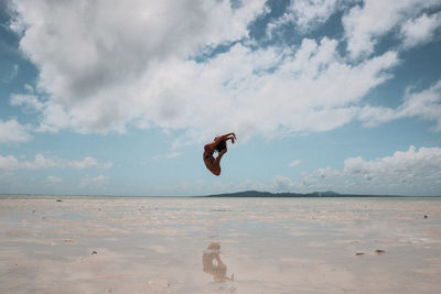 Young woman jumping at beach against cloudy sky