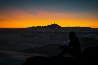 Silhouette man sitting on mountain against sky during sunset