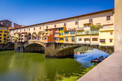 Arch bridge over river against buildings in city against clear blue sky