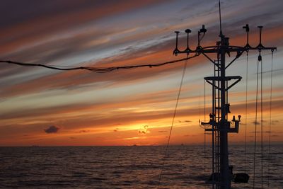 Power lines against sea at sunset