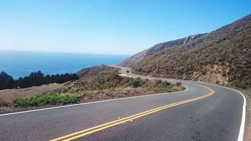 Road by mountain and sea against clear sky