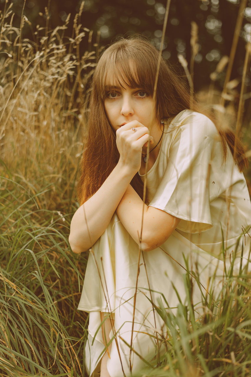 one person, plant, grass, women, child, female, portrait photography, childhood, hairstyle, nature, contemplation, portrait, long hair, field, person, land, photo shoot, young adult, casual clothing, clothing, sunlight, adult, three quarter length, front view, leisure activity, outdoors, looking, brown hair, waist up, looking at camera, day, emotion, spring, dress, blond hair, lifestyles, serious, innocence, human face, skin, teenager, human hair, sadness, standing, human eye, rural scene, summer