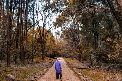 Rear view of woman walking on footpath in forest