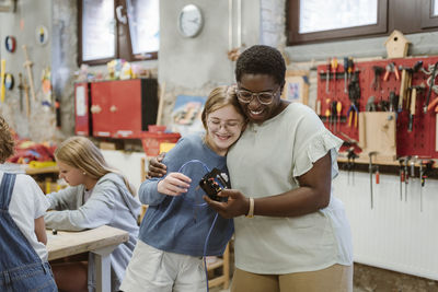 Happy female teacher appraising student while holding electrical part at school workshop