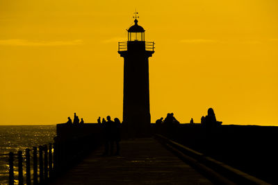 Silhouette lighthouse on pier against sky during sunset
