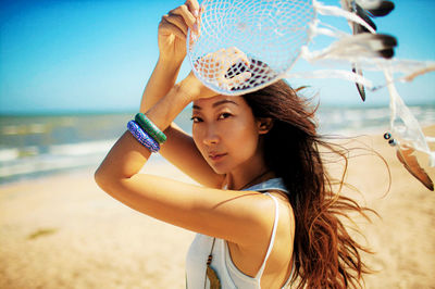 Asian girl with blowing hair holding dream catcher on summer beach.