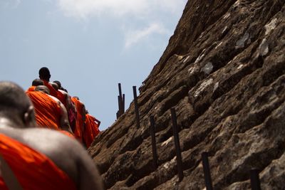 Low angle view of monks climbing on rock formation against sky