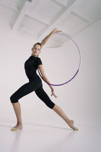 A girl from rhythmic gymnastics in a standing bodysuit shows an exercise with a hoop in a deflection