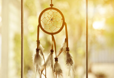 Close-up of dreamcatcher hanging at window against blurred background