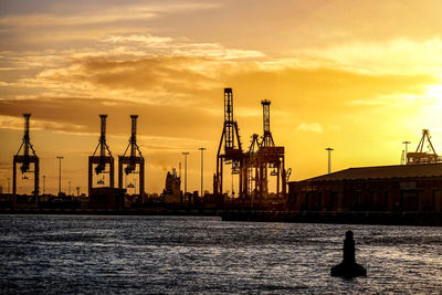 Cranes at commercial dock against sky during sunset