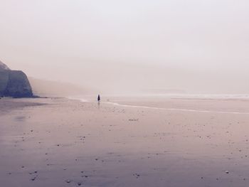 Woman standing at distant on foggy beach