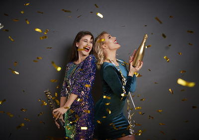 Smiling women with champagne standing against gray background