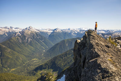 Man on mountain summit looking out at view of forest and peaks.