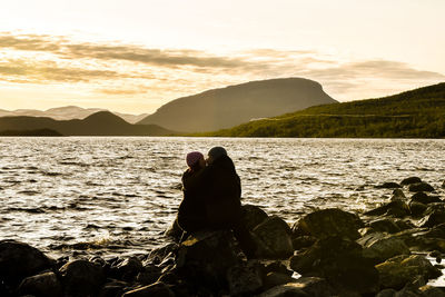 Woman on rock by sea against sky during sunset