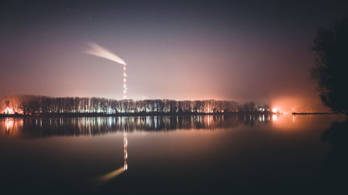 Illuminated smoke emitting from factory against sky at night