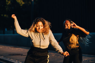 Excited friends dancing at skateboard park during sunset