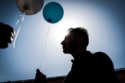 Portrait of young man with balloons against sky