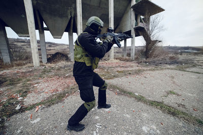 Army soldier aiming while standing against built structure