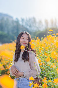 Smiling woman standing by yellow flowering plants