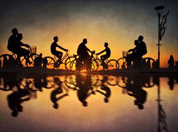 Silhouette people riding bicycles against sky