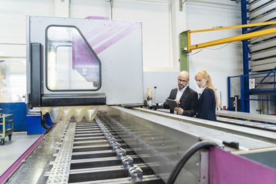 Businessman and businesswoman with tablet at conveyor belt in factory