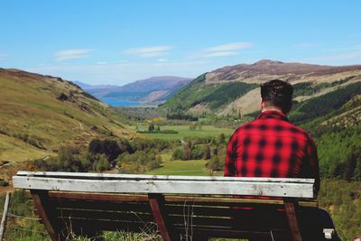 Rear view of man sitting on mountain against sky