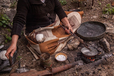 Midsection of woman tinning kitchen utensil by burning fire