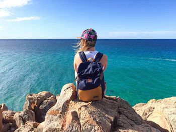 Woman sitting on beach by sea against sky