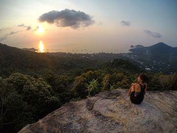 Rear view of young woman looking at sea against sky during sunset