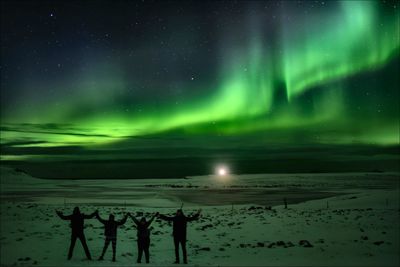 Group of people on snow covered land against aurora polaris