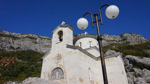 Low angle view of cross by building against clear blue sky