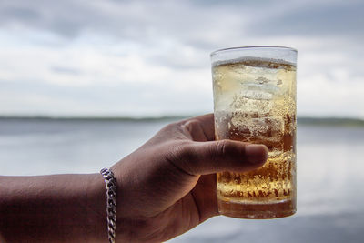 Cropped hand holding drink against sky