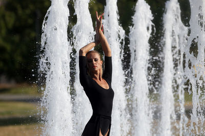 Beautiful woman with hand raised standing against fountain