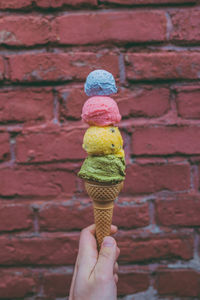 Hand holding ice cream cone against brick wall nicely colored ice cream cone on a sunny day