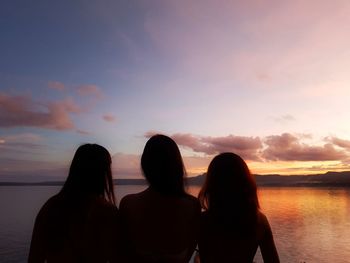 Rear view of silhouette people on beach against sky during sunset
