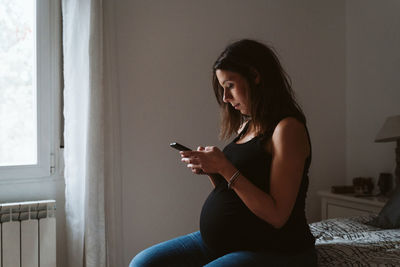 Pregnant woman using phone while resting at home