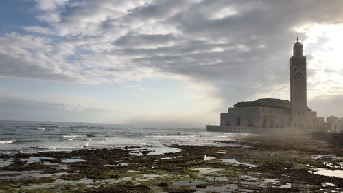 Buildings by sea against cloudy sky